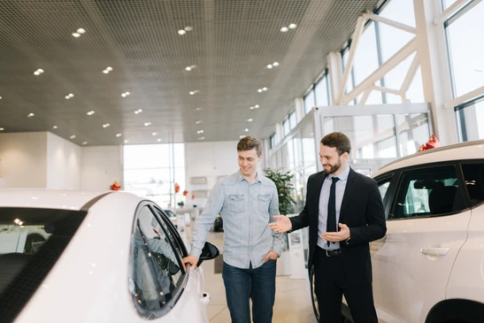 Concession automobile moderne avec vendeur en costume présentant véhicules neufs à client potentiel