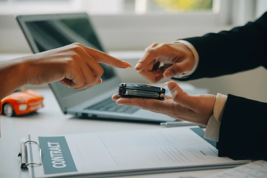 Scène d'intérieur professionnel où deux personnes en costume échangent des clés de voiture au-dessus d'un bureau